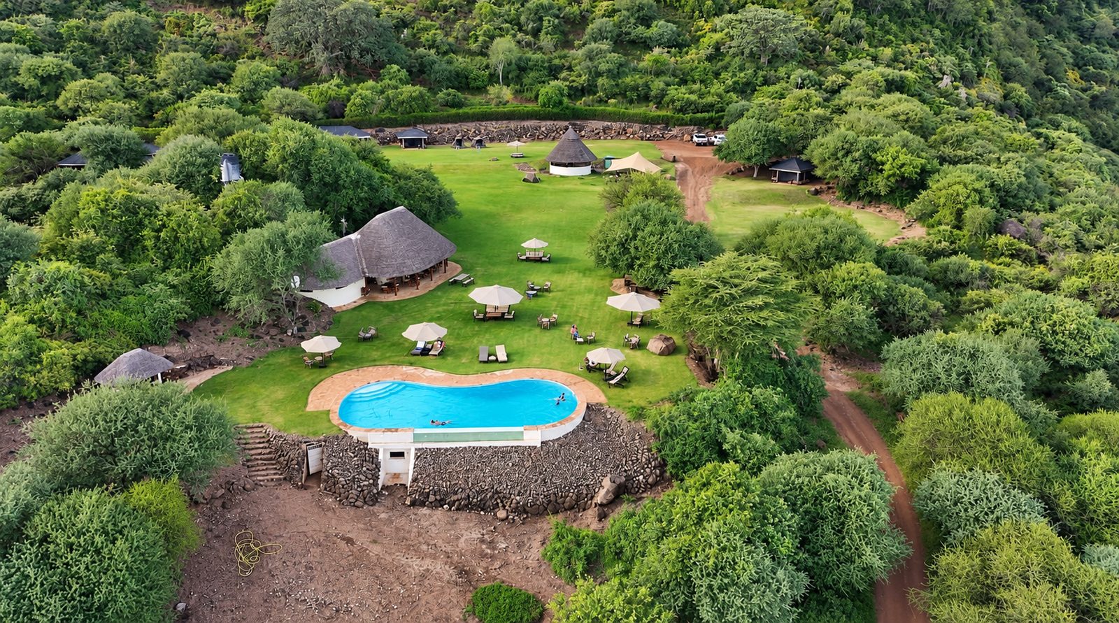 Aerial view of the camp with the pool, lawn and thatched buildings