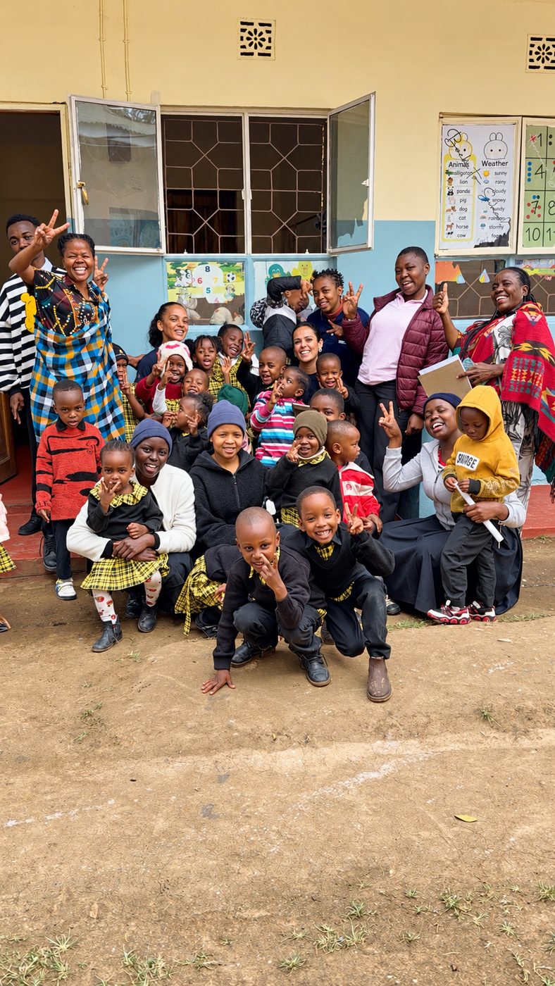 Volunteers and teachers with a classroom of smiling children outside a local school